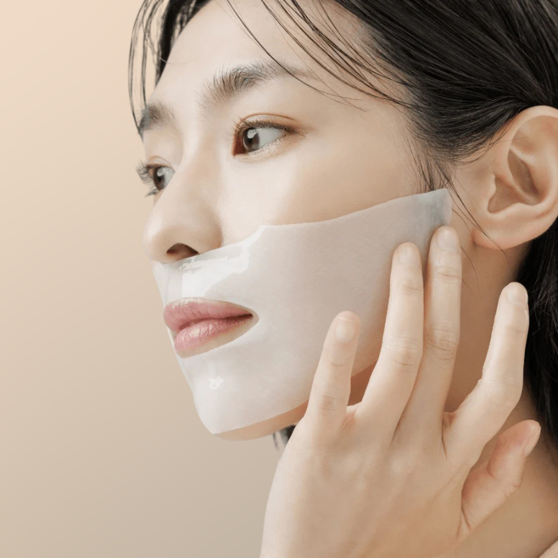 Woman applying a white face mask on a beige background