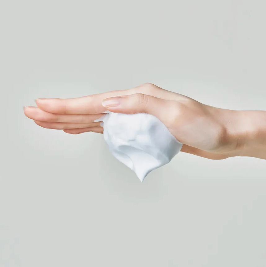 Hand applying white cream to another hand against a light gray background