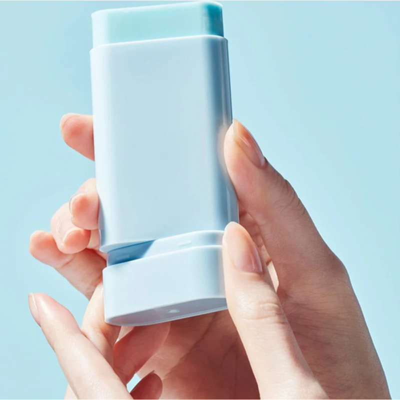 Hand holding a light blue deodorant stick against a light blue background