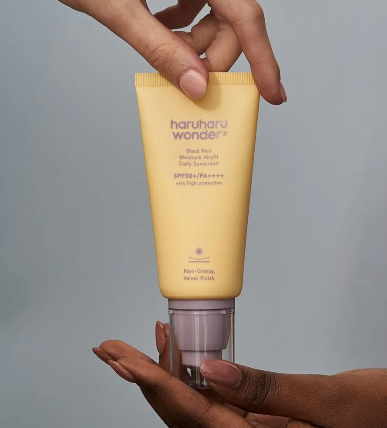 Hand holding a yellow tube of haruharu wonder sunscreen against a gray background