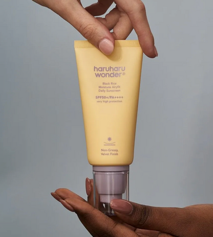 Hand holding a yellow tube of haruharu wonder sunscreen against a gray background