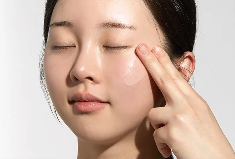 Person applying cream to their face with a neutral background